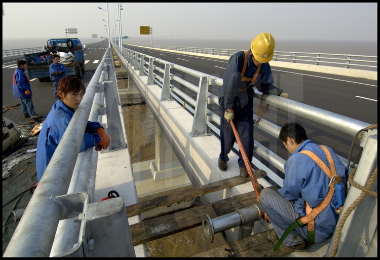 Last finishing works on Donghai bridge roadway at kilometric point 24 (elevation 4). Workers are installing pipes made for rain water evacuation above runways. On background, the main suspended bridge, at kilometric point 16.