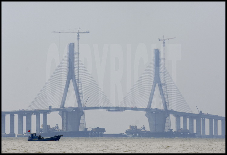 June 2005. Last foundation and binding works on main suspended bridge (roadway height: 40 m), where biggest vessels can get through from Hangzhou bay to Eastern China Sea. Bridge towers are 159 m high for a 420 m width. On foreground, a fishing boat -among many- cruising on Hangzhou Bay.