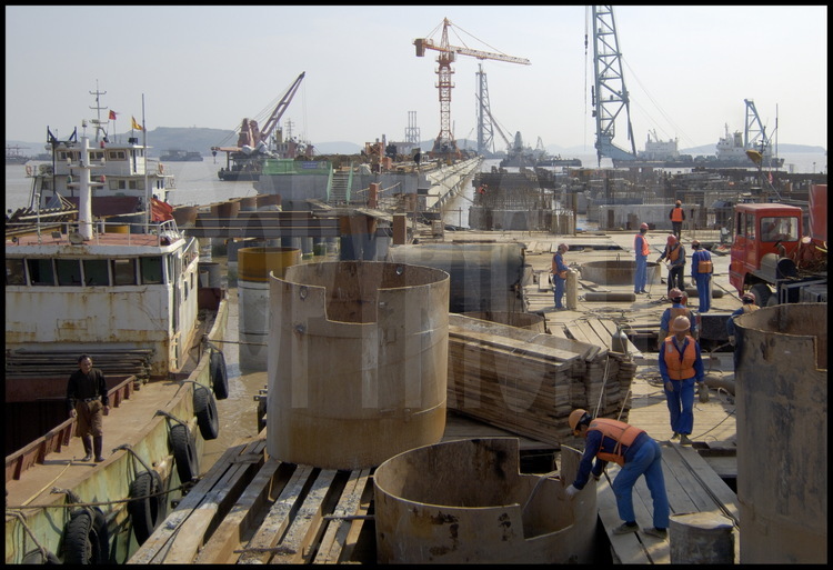 Novembre 2005. Les ouvriers ont commencé à installer les piliers de soutènement de la deuxième phase de travaux du port de Yangshan, gagnée elle aussi sur la mer. Située juste au sud de la première, cette nouvelle tranche sera opérationnelle dès la fin de l'année 2006.  En arrière plan, le sud de l’archipel de Yangshan.