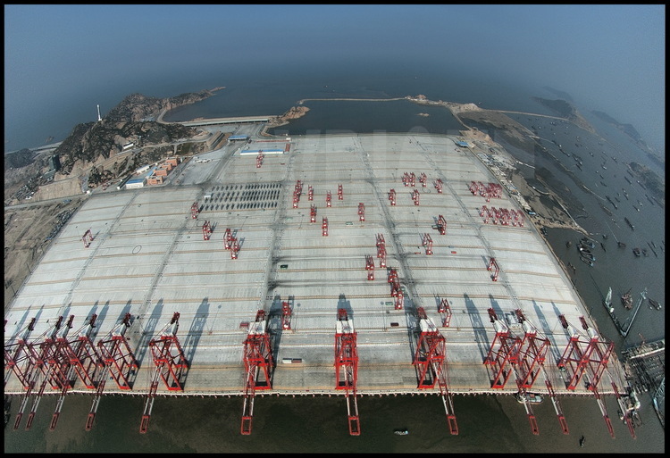 Along this 720000 meter square concrete slab, 1600 meter of wharf. Under, 2819 supporting piles. Above, the fifteen cranes of the first phase, ready to meet world biggest vessels from december 2005. All working station are fully equiped with hi-tech radio recognition container localisation, which makes handling faster (less than 90 seconds for a full take off-landing one) and reduce service mistaking risk. Also, these cranes are able to handle two containers in a row for a maxi weight of 65 tons and a 60 meter range. On left background, the PC harbour center (glass building).
