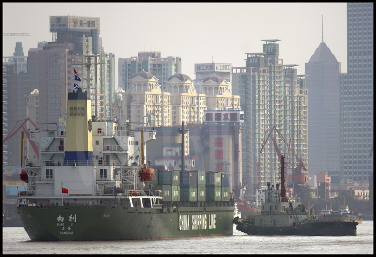 Downtown Shanghai. Helped by a tugboat, a container ship belonging to China Shipping Line (world first company for container traffic) cruising on Huang Pu river. On background, towers of the new city of Pudong (meanings 
