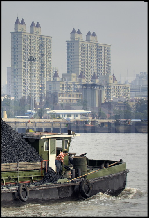 In downtown Shanghai, a barge carrying coal cruising on Huang pu river. On background, habitation towers of Puxi (meanings 