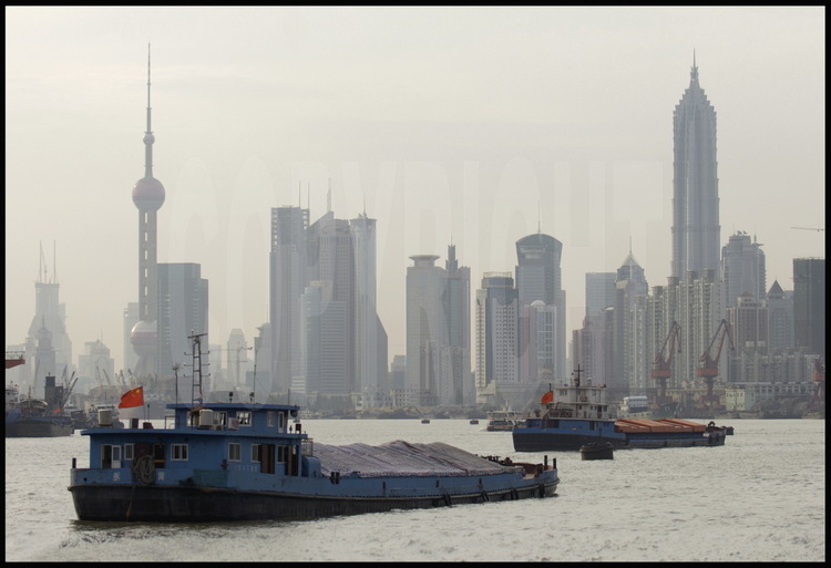In downtown Shanghai, barges cruising on Huang Pu river. On background, towers of the new city of Pudong (meanings 