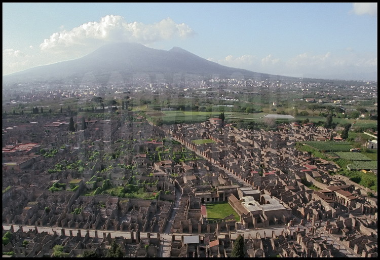 Aerial view of Pompeii’s center. In the foreground on the right, the intersection of the ancient city’s two main arteries, Via del Vesuvio and via dell’Abondanza, home to the Stabies baths.  In the background, Mt Vesuvius.
