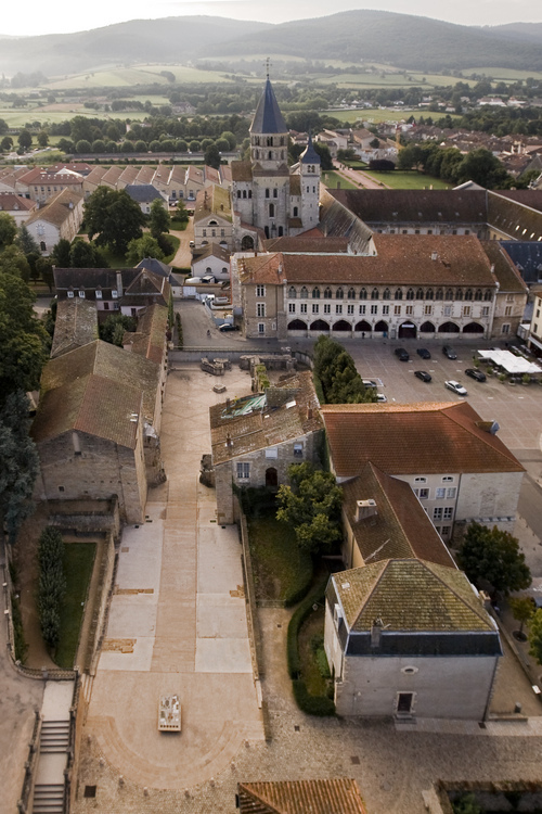 Cluny : Au sol, vestiges de l'ancienne basilique disparue à la Révolution. En arrière plan, l'abbaye et le clocher de l'Eau-Bénite.