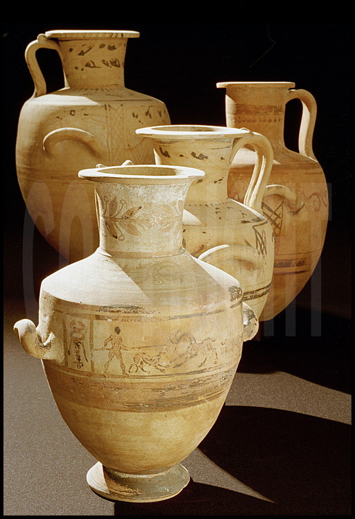 Habituellement destinées à contenir de l'eau, ces vases, fabriqués dans la proche cité d'Hadra -nommées hydries d'Hadra- ont été retrouvés en parfait état de conservation. Ils servaient à Necropolis d'urnes cinéraires : la plupart d'entre eux ont été retrouvés avec les cendres du défunt toujours à l'intérieur. Sur le vase du premier plan, une scène peinte de facture particulièrement originale, avec  chasseur, lévrier et cervidé. IIIème siècle avant J.C..