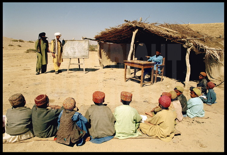Village and school of Sartaf. For the occasion, Jean Loup Welcomme plays schoolteacher. He explains to the children why he has come to their village, and how the desert in which they live was a lush forest 30 million years ago, where great creatures like Baluchitherium roamed. Background, left to right: Kehar, Bugti expedition leader and native of Sartaf; Jean Loup Welcomme as the teacher at the blackboard.