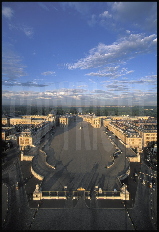 Vue aérienne du Château de Versailles. Au premier plan, l’entrée du château et la Grille Royale, puis la Cour des Ministres où trône la statue équestre de Louis XIV, la Cour Royale et la Cour de Marbre. En arrière plan, la grande perspective donnant sur le Grand Canal.