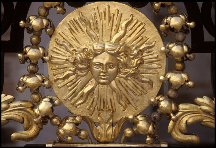 Sur la grille du balcon de la chambre du Roi, Emblème royal : tête d’Apollon ornée de guirlandes fleuries.