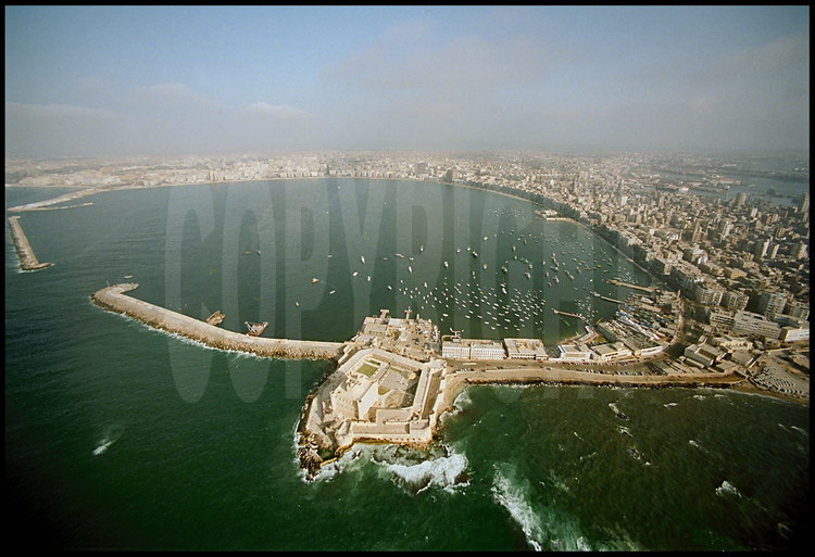 Overall view of the Eastern Port and of downtown Alexandria.  In the foreground, Qaitbay Fort, built on the ancient lighthouse’s site by sultan Mamelouk Ahray Qaitbay at the end of the fifteenth century (1477).  On the left of the fort, the underwater digging site where the blocs of the ancient lighthouse were discovered.