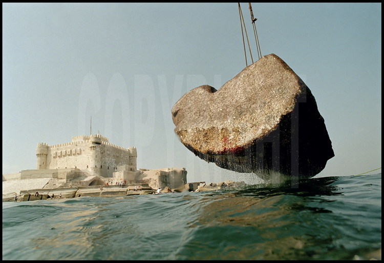 Restoration of one of the sixty-ton blocs which surrounded the ancient lighthouse’s entrance door.  Today, its height is estimated at twelve meters.  In the background, Qaitbay Fort , built in the fourteenth century on the lighthouse’s site.