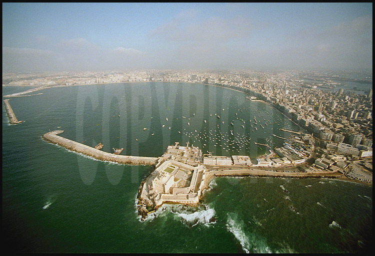 Overall view of the Eastern Port and of downtown Alexandria.  In the foreground, fort Qaitbay, built on the ancient lighthouse’s site by Sultan mamelouk Ahray Qaitbay at the end of the fifteenth century (1477).  On the left of the fort, the underwater digging site where the blocs of the ancient lighthouse were discovered.