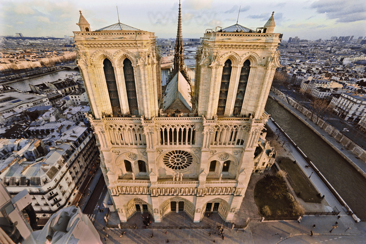 The west facade of Notre Dame in late afternoon, Ile de la Cité. On the court, the zero kilometer point, which marks the intersection of the roads of France. In the center, the arrow (rebuilt in the nineteenth century on the foundations of the old, shot in the Revolution) is 96 meters and towers 69 meters. Narrow and very high bays (over 16 meters) give them lightness. The façade is 43.5 meters wide. At the foreground, l. to r., Arcola street, the square of Notre Dame, the south arm of the Seine and Quai de Montebello. On the back ground l. to r., the church of Saint Gervais and the Latin Quarter. Altitude 60 meters.