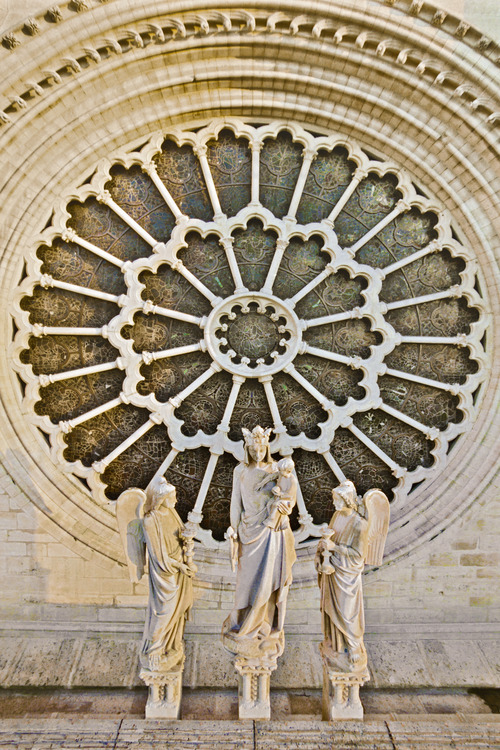 Level of the Rose. At the center of west facade, Notre Dame, the Virgin to whom the cathedral is dedicated. The statue of the Virgin Mary stands in the center of the facade, front to the rose, to welcome the 20 million of visitors who tread the square each year. Accompanied by two angels, Christ Child holds in his hand a pomegranate, the fruit of love. With nearly 10 meters in diameter, the large Rose was long the more larger than builders have dared to assemble. Its design is so perfect that none of its components moved for more than seven centuries. View from the square, it forms like an aureole to the Virgin. Altitude 27 meters.