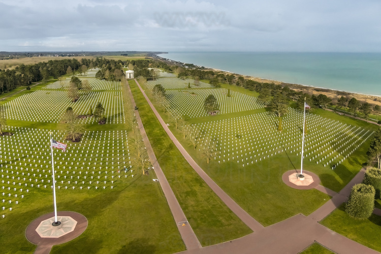 Normandie - Calvados (14) - Colleville sur Mer : Site 3 : Cimetiere americain de Colleville sur Mer. Inaugure officiellement en 1956, cette necropole de 70 hectares est installee sur les hauteurs qui surplombent la plage d'Omaha Beach. Il a ete concu par Harbeson, Hough, Livingston & Larson et l'espace a ete arrange par l'architecte paysagiste Markley Stevenson qui a fait en sorte que, de n'importe quel angle, on voit une rangee de croix. A l'entree du cimetiere, une statue en bronze de 7 metres de haut, a l'interieur du demi-cercle forme par la colonnade du memorial, fait face aux carres des tombes. Elle symbolise l'Esprit de la jeunesse americaine s'elevant des flots. Cette statue est entouree de galets symbolisant la difficulte des tanks a passer la plage. Les steles de marbre blanc sont en forme de croix latine ou en forme d'etoile de David pour les soldats de confession juive. Dans le cimetiere sont enterres les corps de 9 388 personnes, dont 307 inconnus et quatre femmes. Ces personnes sont principalement decedees le jour du debarquement ou dans les semaines suivantes en Normandie, principalement au combat. 14 000 depouilles, d'abord inhumees en Normandie, ont ete rapatriees aux Etats-Unis, a la demande de leurs proches. 3 titulaires de la Medal of Honor morts en Normandie reposent a Colleville, dont le general Theodore Roosevelt Junior (1887-12 juillet 1944, fils aine du president des Etats-Unis Theodore Roosevelt et lointain cousin du president Franklin Roosevelt). Deux des freres Niland, dont l'histoire a inspire Steven Spielberg pour ecrire le scenario du film 