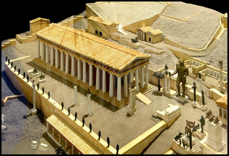 Représentation du centre du sanctuaire d’Apollon à Delphes. Au centre, le temple d’Apollon érigé au IVe s. av. J.C. A droite, la statue colossale du dieu Apollon par le sculpteur Sitalcas. En arrière plan, l’amphithéâtre construit également au 4e s. av. J.C.