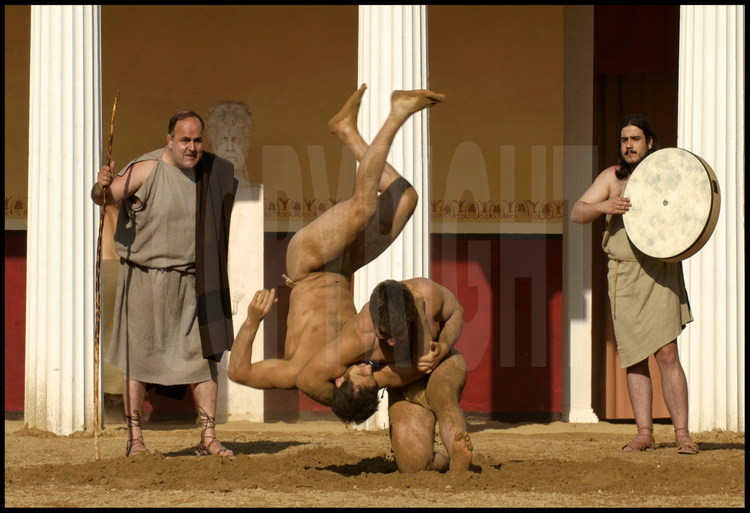 During Antiquity, athletes trained to the sound of the drum and the aulos.  Watched by Greek trainer Christos Kollias and the musician, Stefanos Tsanoulas (left) and Theofanis Anagnostou train for the wrestling event in the palestra’s courtyard.
