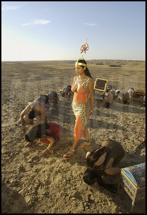 L’épouse du pharaon, vêtue de ses attributs royaux, l’aide dans sa quête. Métamorphosée en déesse Seshat, la divinité gardienne des mesures et des écrits, elle immortalise l’acte de fondation de la pyramide.