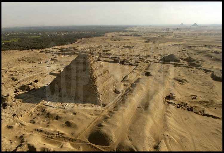 Vue aérienne de la nécropole de Sakkarah depuis le Nord. Au premier plan, la pyramide de Djoser (IIIème dynastie), plus ancien monument bâti en pierre de l’histoire. Elle fut édifiée par le génial architecte Imhotep et restaurée par l’équipe du français Jean Philippe Lauer. Au second plan, la chaussée et la pyramide d’Ounas (Vème dynastie). En arrière plan à gauche, l’oasis occidental de la vallée du Nil et le site ou était située Memphis, l’ancienne capitale des pharaons de l’Ancien Empire. En arrière plan à droite, les pyramides rhomboïdale et rouge de Dashour (IVème dynastie) construites par Snéfrou, père de Kheops.
