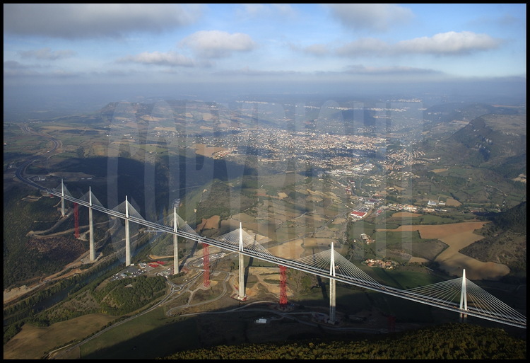 End of October 2004 : building phase is completed. Before the grand opening planned on December 14th, workers are going to take down the temporary structures (in red) and link the roadway to each motorway rim. On the left background, the Causse Rouge, on the center Millau city, on the right, the Causse du Larzac.