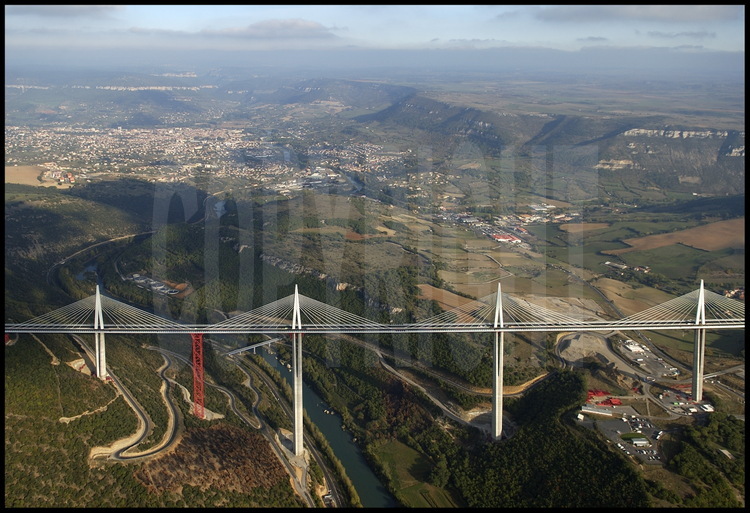 End of October 2004 : building phase is completed. Before the grand opening planned on December 14th, workers are going to take down the temporary structures (in red) and link the roadway to each motorway rim. On the center background, Millau city, on the right the Causse du Larzac.