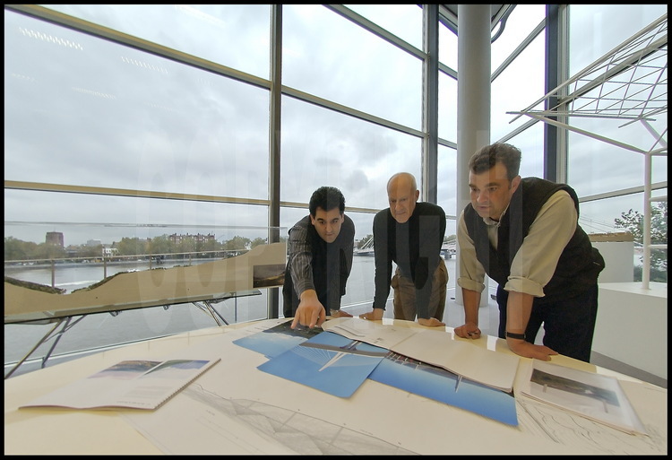 Dans ses bureaux du quartier de Battersea à Londres, Sir Lord Norman Foster et ses directeurs de projet Mouzhan Majidi et Alistair Lenczner étudient et commentent des photographies et des plans du Viaduc de Millau. En arrière plan à gauche, la maquette du Viaduc de Millau et la Tamise.