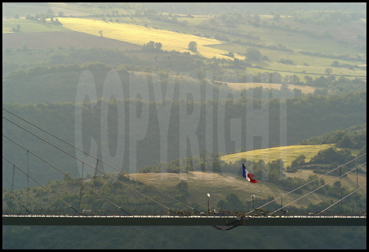 Vendredi 28 mai, fin de journée. Culminant à 268 mètres au dessus du Tarn, le drapeau français flotte au dessus du point de jonction des deux parties du tablier métallique. En arrière plan, le Causse Rouge.