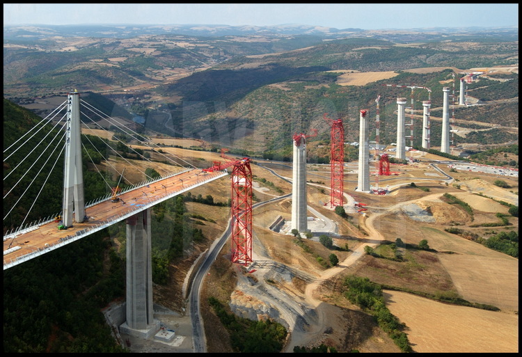 General view of the viaduct’s construction site in June, 2003.  The first part of the metallic roadway, 342 meters long, is launched above the Tarn valley at a rate of 6 meters per hour.  After joining the temporary pillar (in red) 171 meters away, the roadway is “pushed” towards pier P6, 171 meters ahead.  In the background, the Red Limestone Plateau.